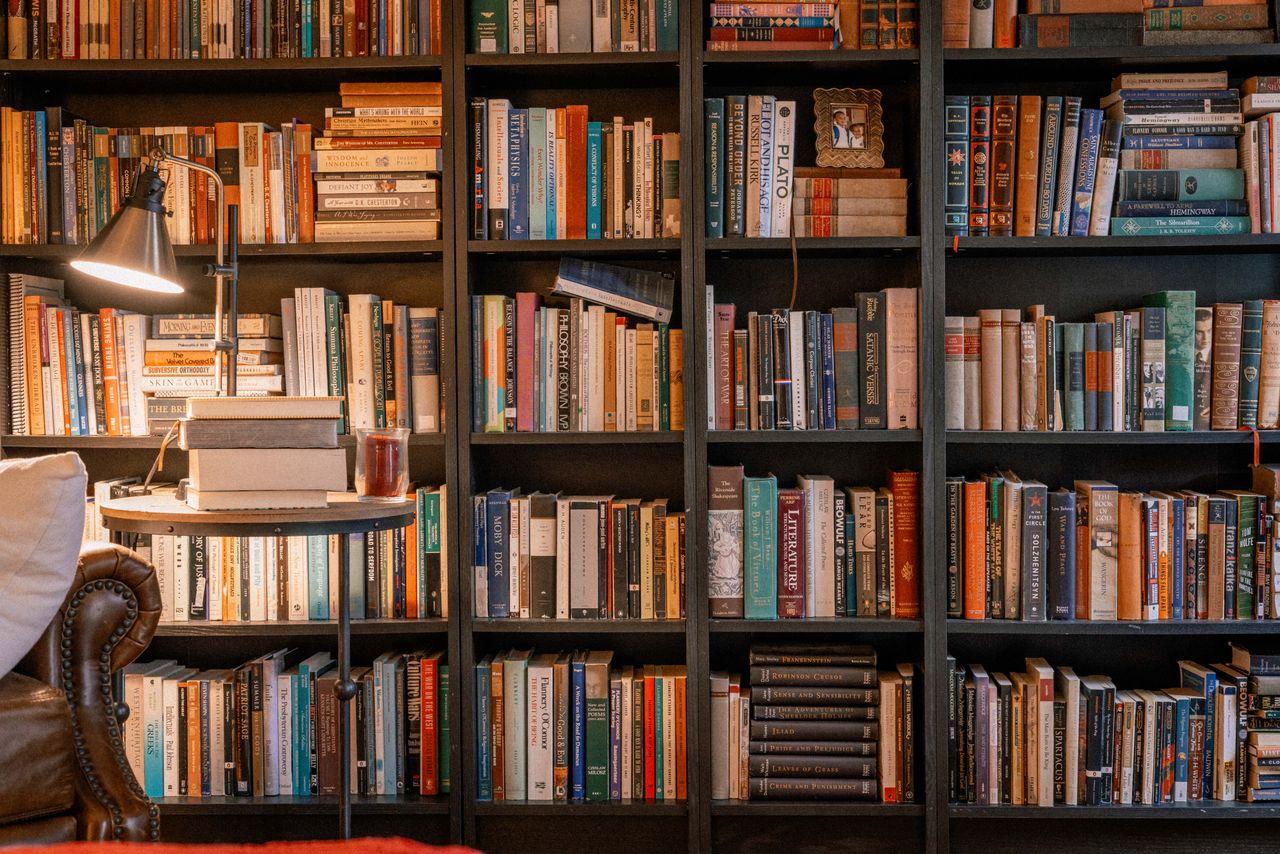 A warm, inviting library scene featuring a bookshelf, books, and a reading lamp.